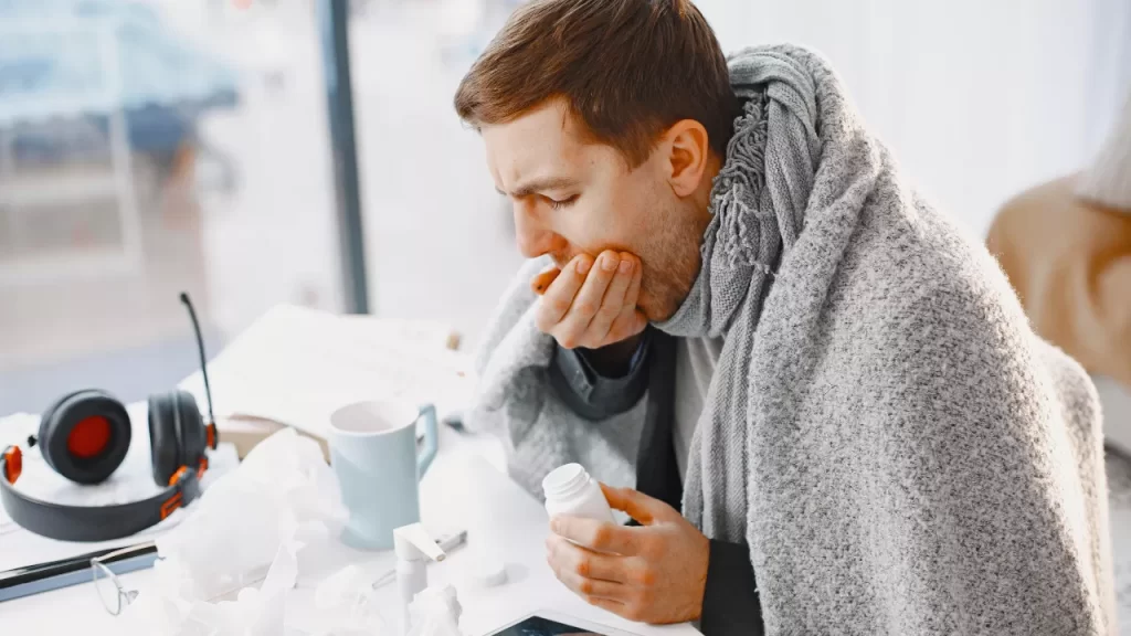 Adulto com gripe enrolado no cobertor tomando chocolate quente.
