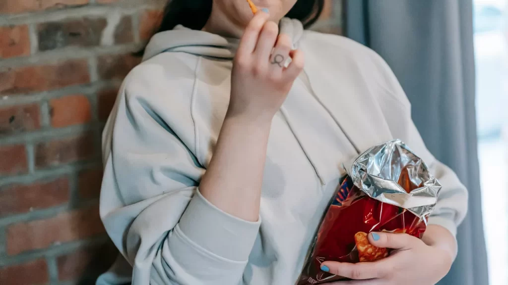 Pessoa comendo salgadinho ultraprocessado, um dos produtos com selo da anvisa que exige moderação.